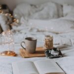 a layout of coffee, book on a bed with fairy lights indicating a cozy morning routine